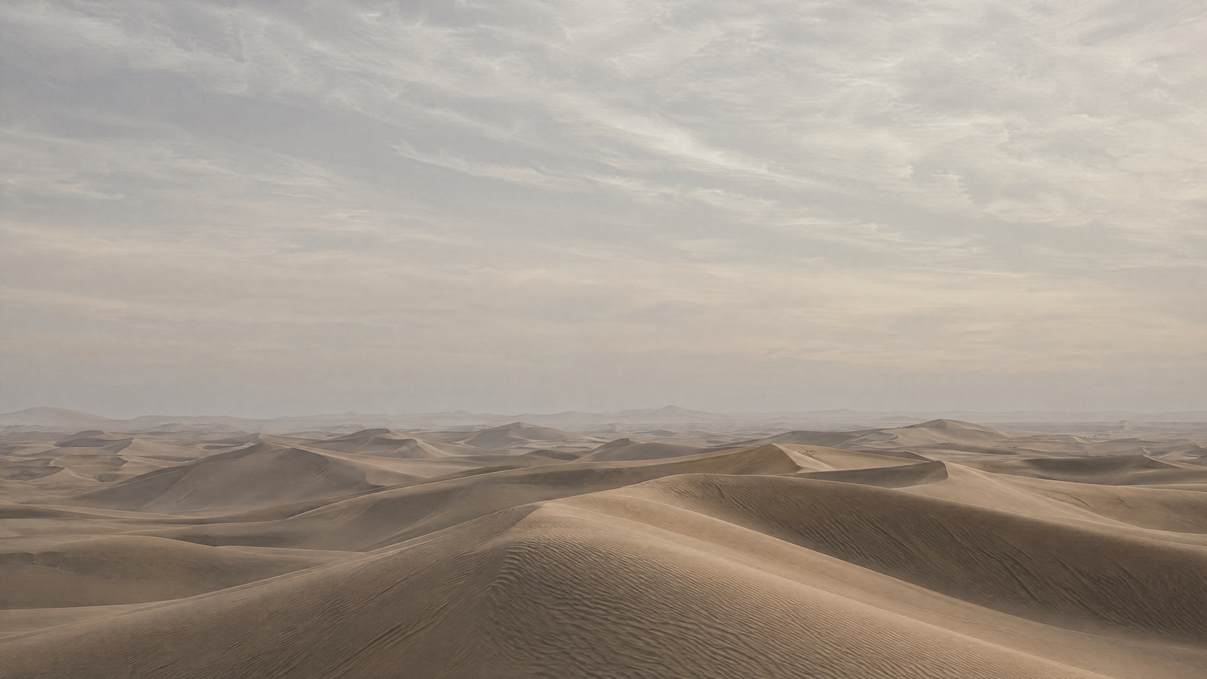 Wind-shaped sand dunes under a soft, overcast desert sky